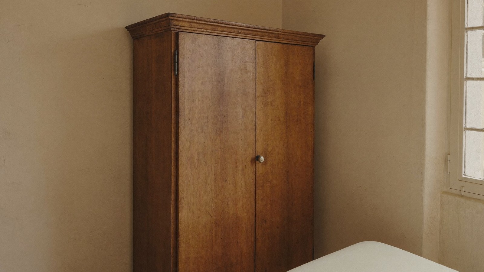 Armario de madera cerrado contra una pared exterior en un dormitorio con luz fría de mañana