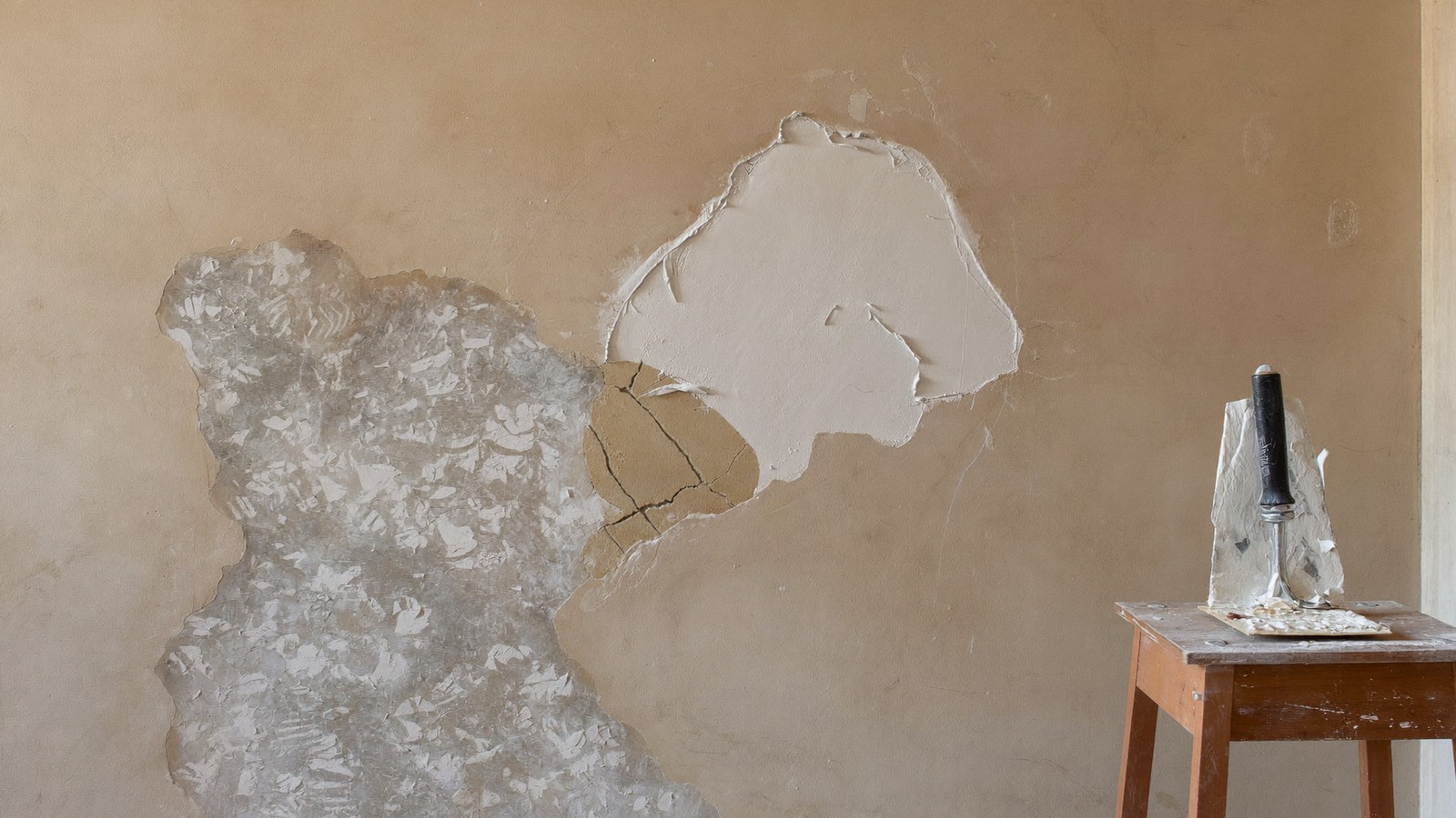 Pared en plena reparación con pintura levantada retirada y masilla fresca aplicada