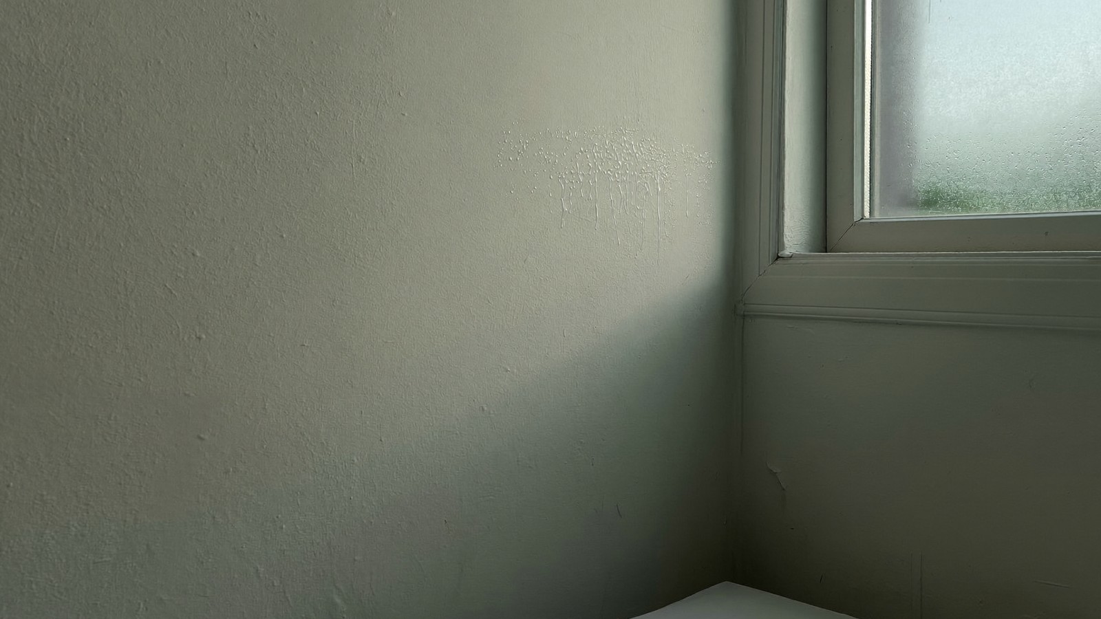 Rincón de dormitorio junto a una ventana con gotas de condensación formándose sobre la pared fría