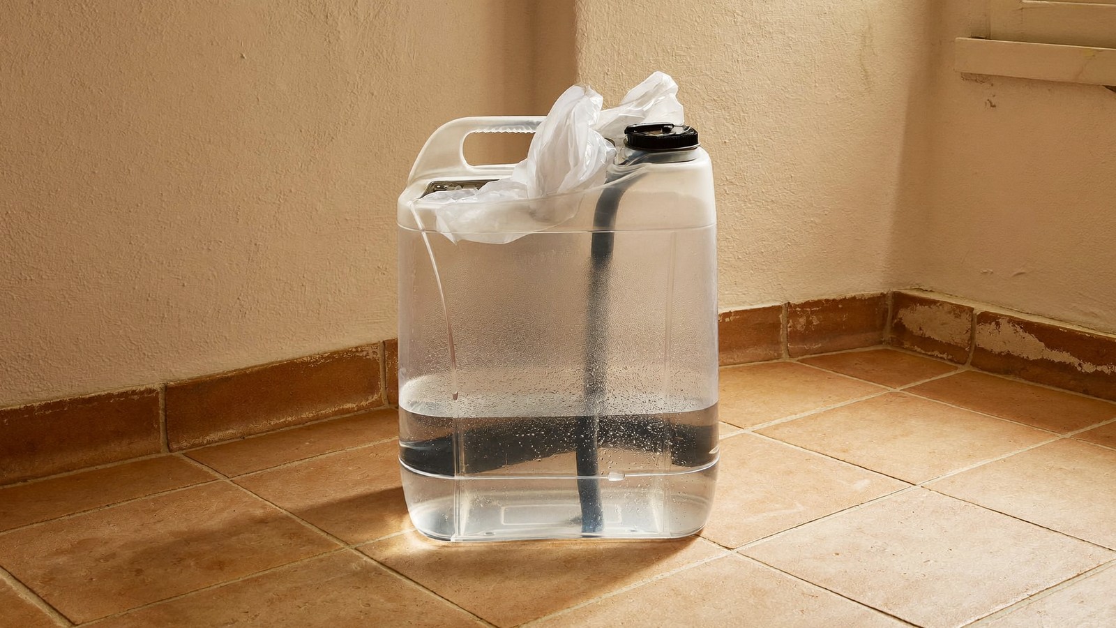 Depósito transparente con el agua recogida del aire de una habitación, sobre suelo de barro cocido