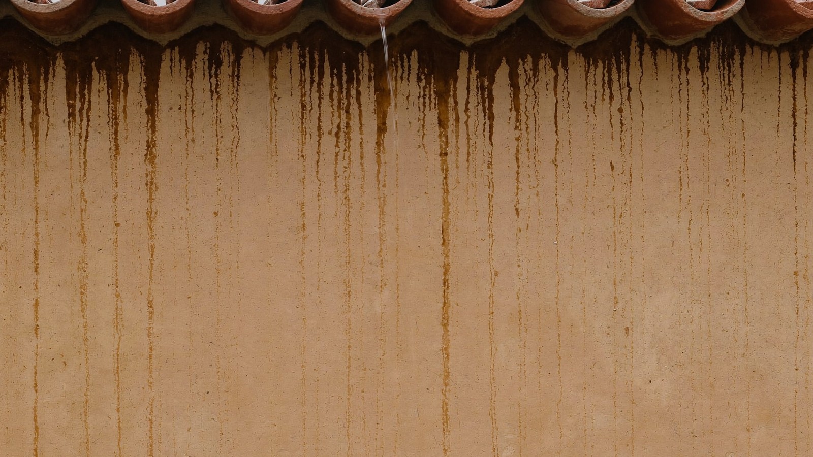 Regueros de agua de lluvia oscureciendo el revoco de una fachada bajo las tejas