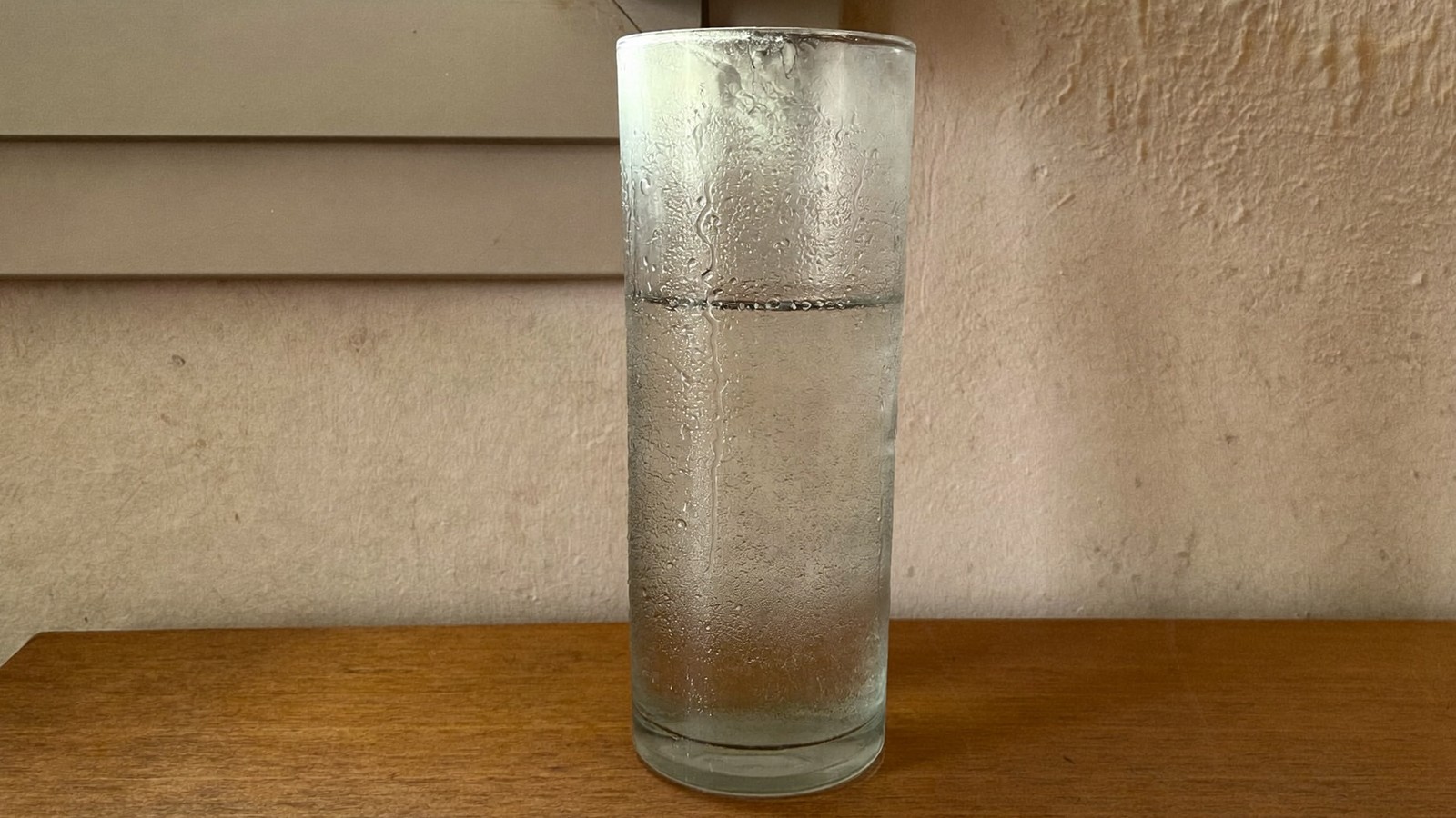 Vaso de agua fría cubierto de condensación sobre una mesa de madera, señal de aire cargado de humedad