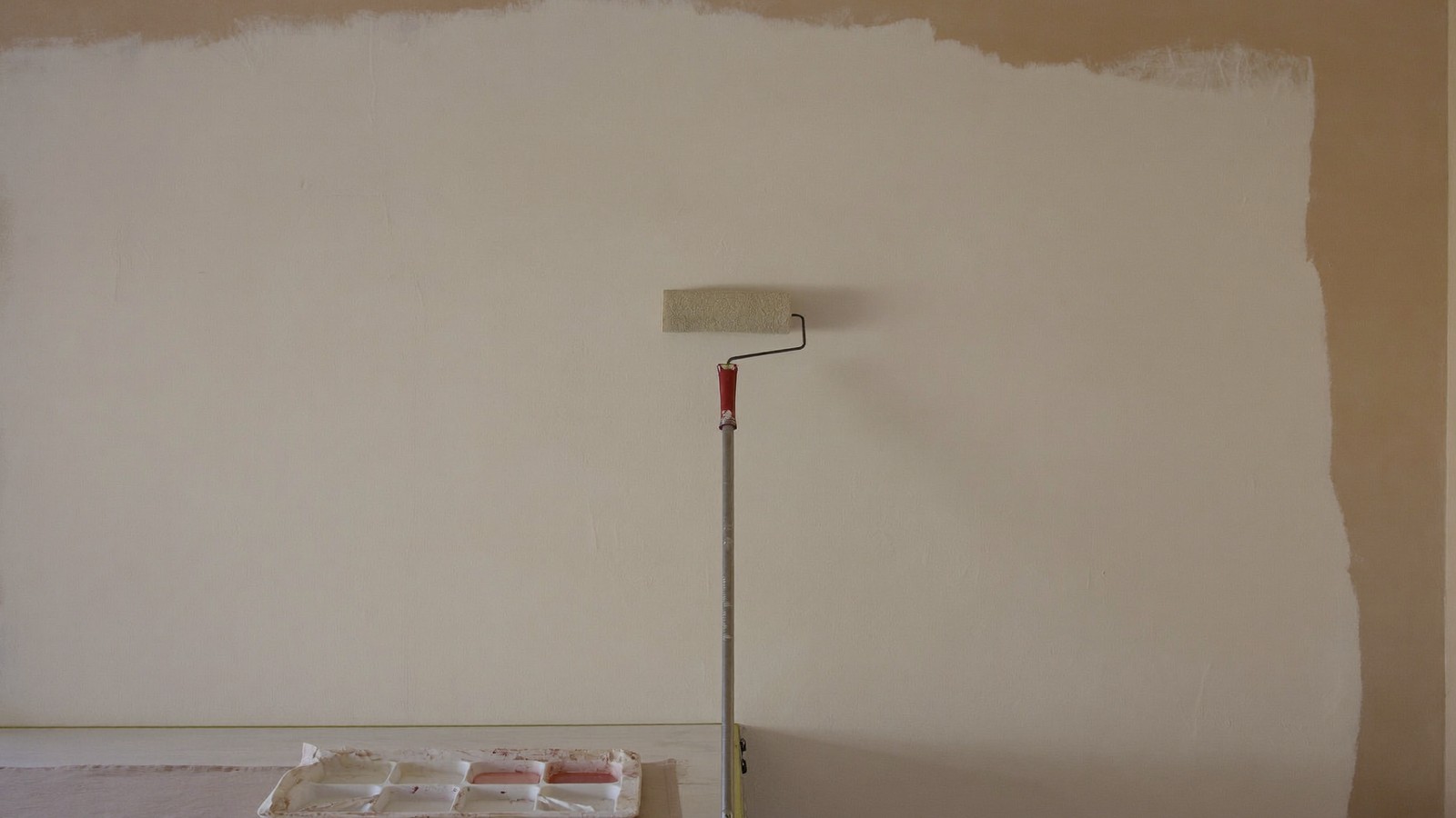 Rodillo aplicando pintura clara sobre una pared preparada, con parte del fondo aún sin cubrir