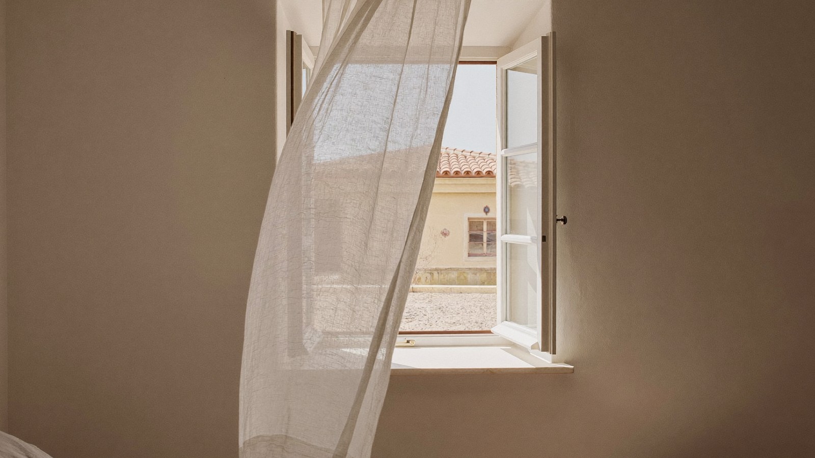 Dormitorio ventilándose por la mañana con la ventana abierta y la cortina movida por la corriente