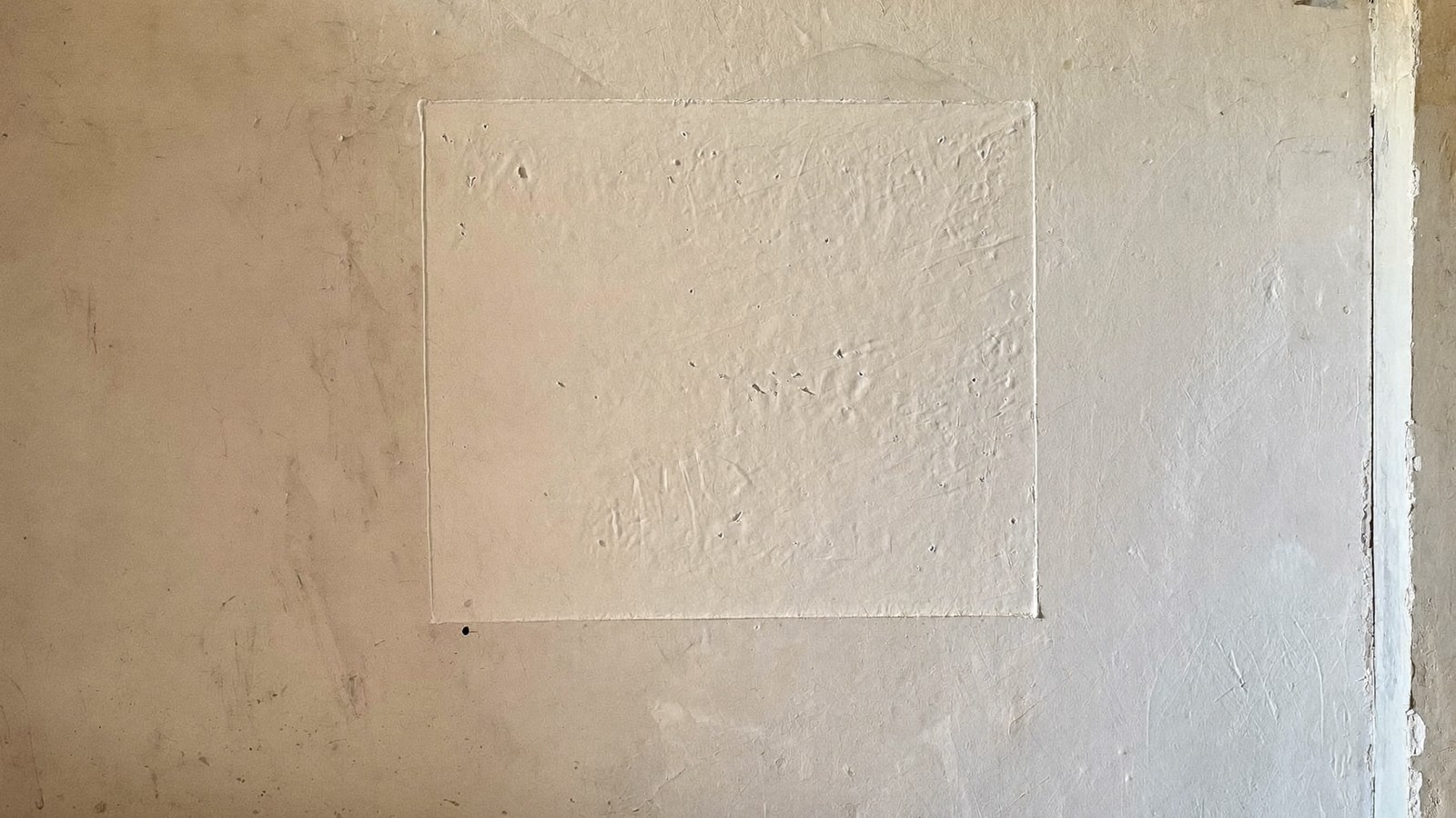 Parche de masilla blanca recién aplicado secándose sobre una pared de yeso antigua