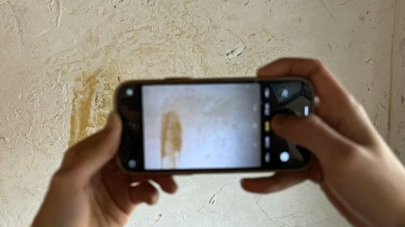 Manos sujetando un móvil en horizontal para fotografiar una mancha de humedad en la pared
