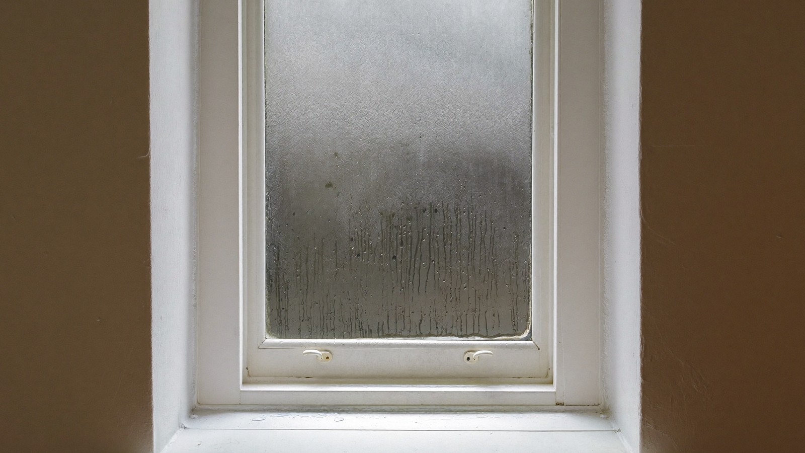 Ventana empañada por condensación con gotas resbalando hasta el alféizar blanco