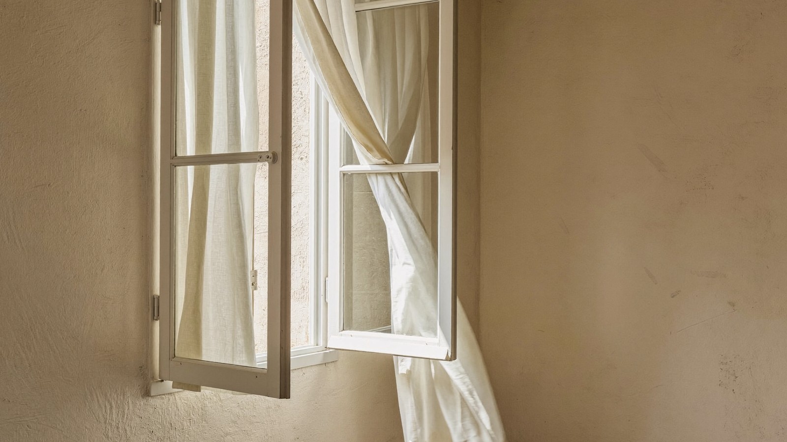 Ventana batiente abierta hacia el interior con luz de mañana cruzando la habitación